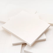 Ein Stapel leerer Notizblockseiten von Alexandra Renke mit subtilen Raster- und Punktmustern auf weißem Papier, ideal für Bullet-Journal-Setups, arrangiert in weichem Licht.