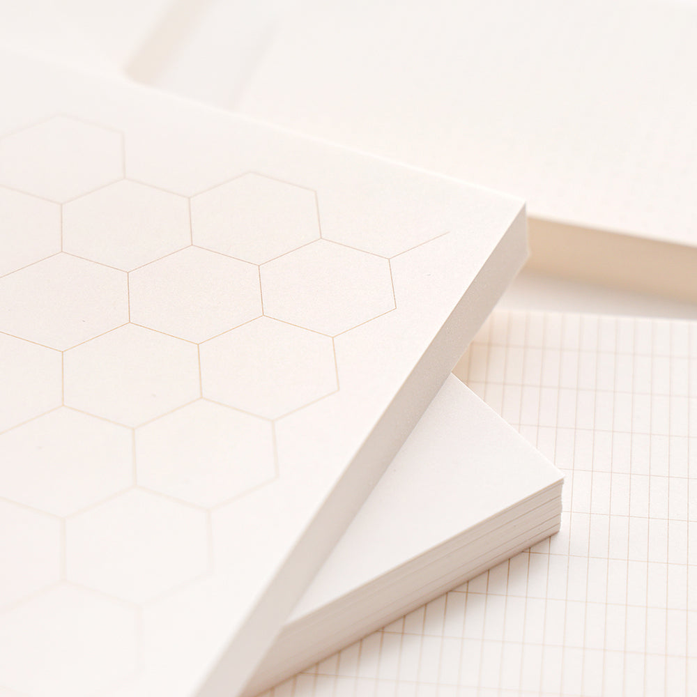 Nahaufnahme eines gestapelten Alexandra Renke Notizblocks und loser Blätter mit Sechseck-, Gitter- und Linienmustern - ideal für Ihre Bullet-Journal-Ideen.