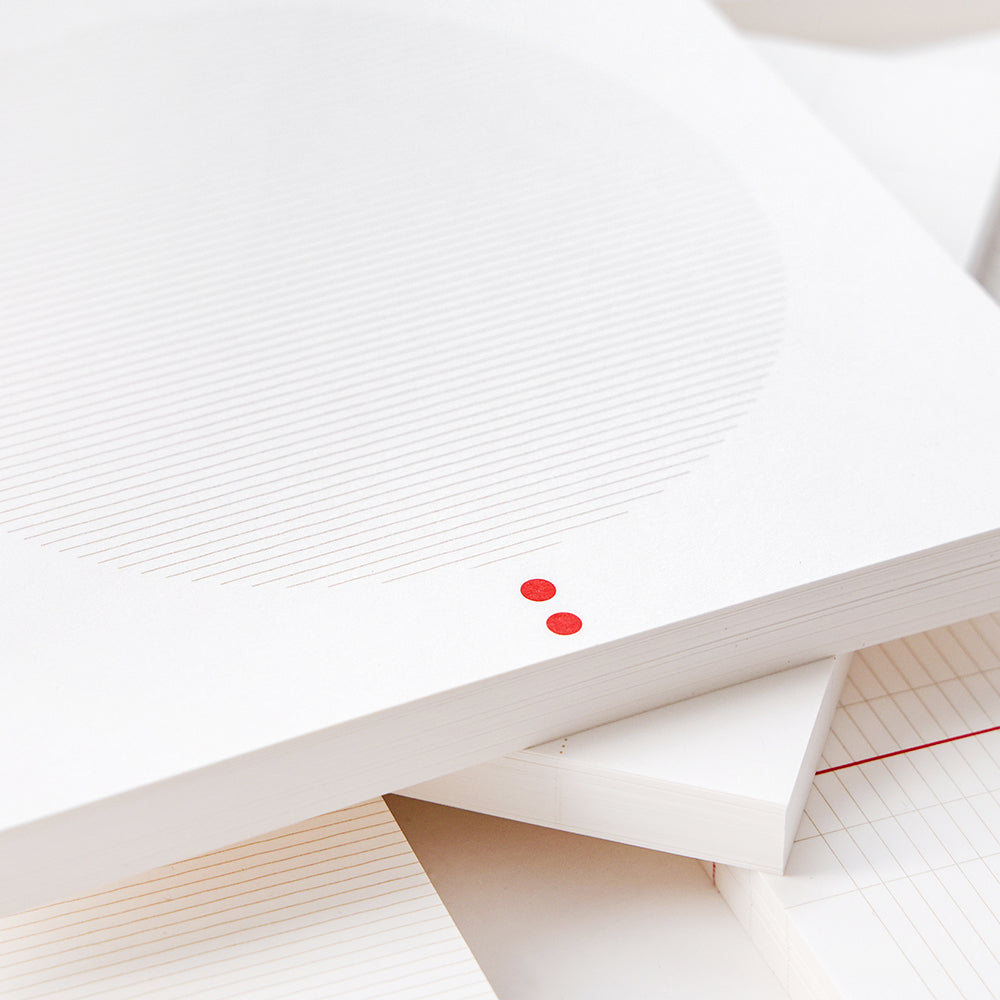 Ein weißer Notizblock von Alexandra Renke mit dünnen Linien in einem Kreis und zwei kleinen roten Punkten am Rand, gestapelt auf losen Blättern - perfekt für Bullet-Journal-Fans.