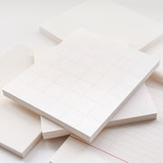 Ein Stapel Blanko-Notizblöcke von Alexandra Renke und lose Blätter in Raster-, Linien- und Punktmustern, die alle aus hochwertigem weißem Papier hergestellt sind.