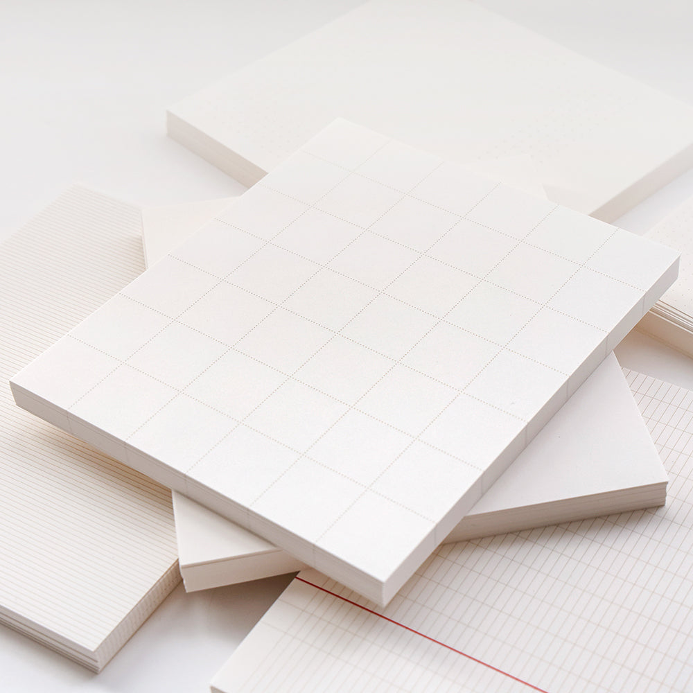Ein Stapel Blanko-Notizblöcke von Alexandra Renke und lose Blätter in Raster-, Linien- und Punktmustern, die alle aus hochwertigem weißem Papier hergestellt sind.