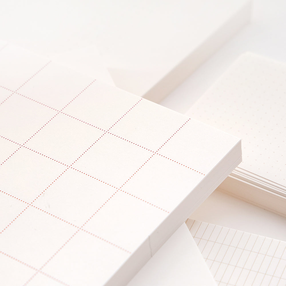 Stapel von weißen Alexandra Renke Notizblöcken und losen Blättern mit Gitter- und Punktmustern in weichem, neutralem Licht - ideal für Bullet-Journal-Inspirationen.