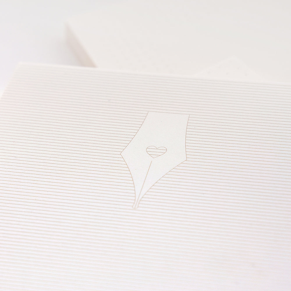 Minimalistische Nahaufnahme einer Füllfeder mit einem Herzdetail, geprägt auf einer weißen, gefütterten Alexandra Renke Bullet-Journal oder Notizblock Oberfläche.