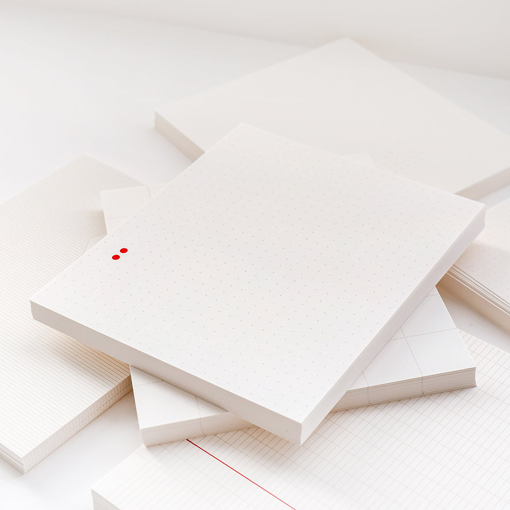 Ein Stapel weißer Lose-Blatt-Notizblöcke von Alexandra Renke in verschiedenen Raster- und Punktmustern, ideal für Bullet-Journal-Setups, ausgestellt auf einer weißen Fläche.