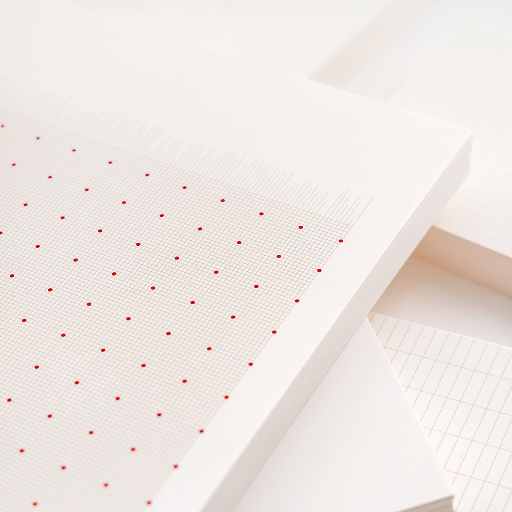 Nahaufnahme der losen Blätter eines Alexandra Renke Notizblocks, mit weißen Seiten mit roten und grauen Gitter- und Punktmustern - perfekt für Ihr nächstes Bullet-Journal.