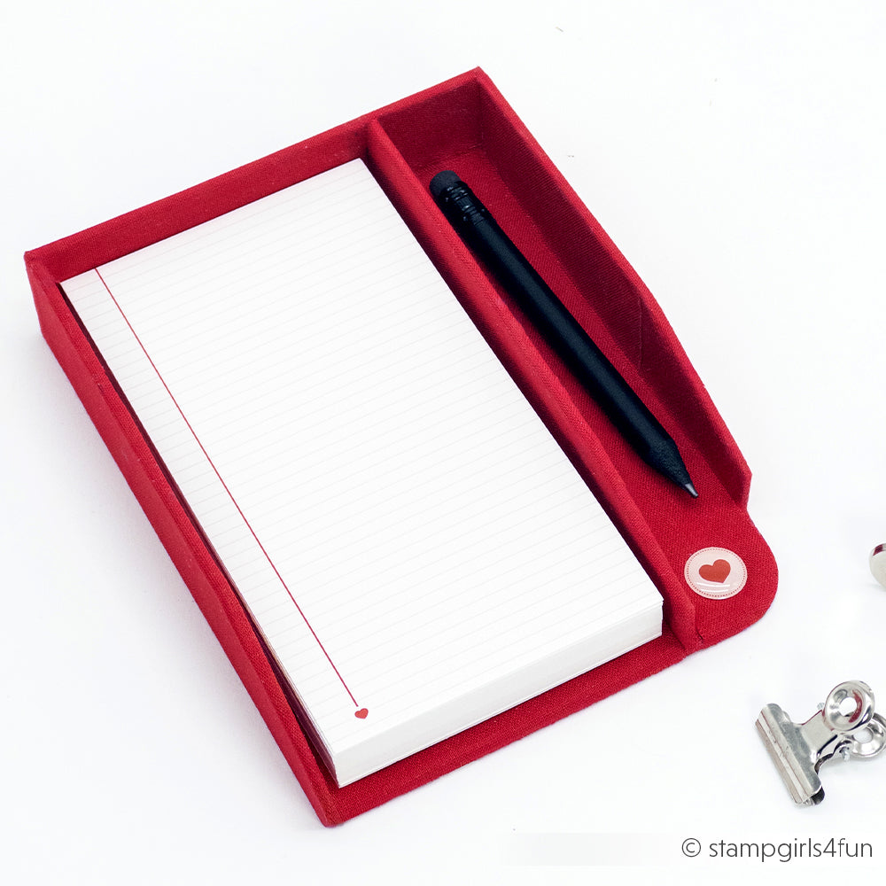 Ein schwarzer Alexandra Renke Kugelschreiber und linierte Notizkarten in einem roten Halter mit Herzknopf sowie ein Metallclip - perfekt für Ihr Bullet-Journal oder zum Ordnen loser Seiten.