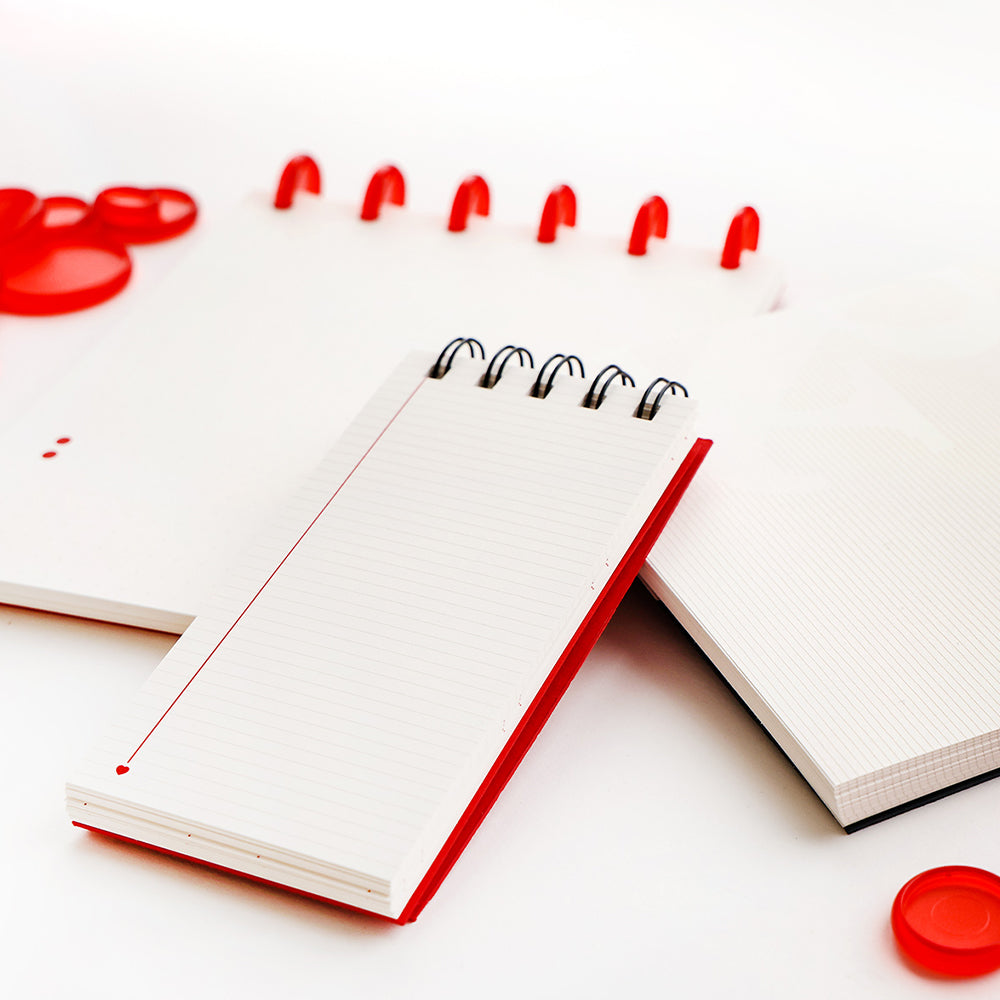 Drei Alexandra Renke Spiralhefte mit roten Akzenten, ideal für Bullet-Journal-Fans, zusammen mit roten Plastikstiften auf einer weißen Oberfläche.