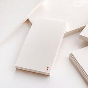 Ein weiß gepunkteter Notizblock von Alexandra Renke, perfekt für Bullet-Journal-Fans, zeigt zwei kleine rote Punkte in der Ecke und ist umgeben von losen Blättern und anderen weißen Papieren.