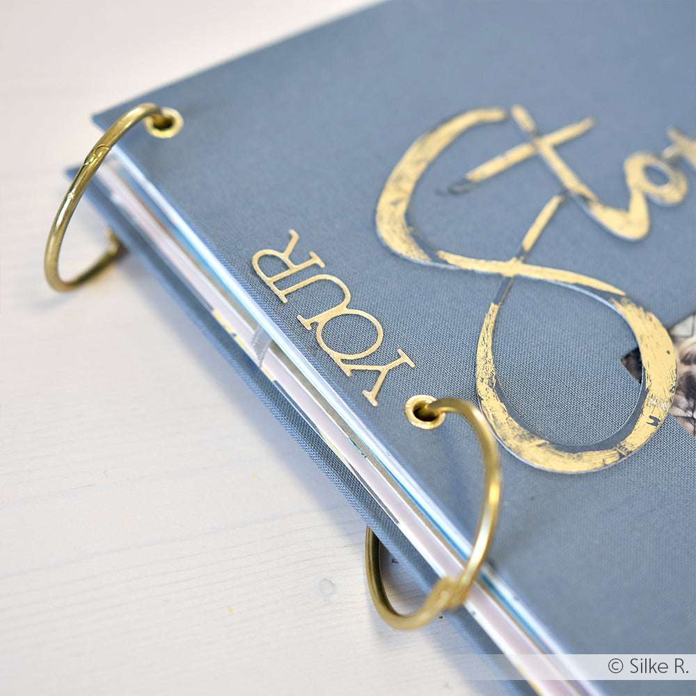Ein blaues ☆ Minialben-Sammelalbum mit goldenen Buchringen und IHRER Geschichte in eleganter Goldschrift auf dem Einband.