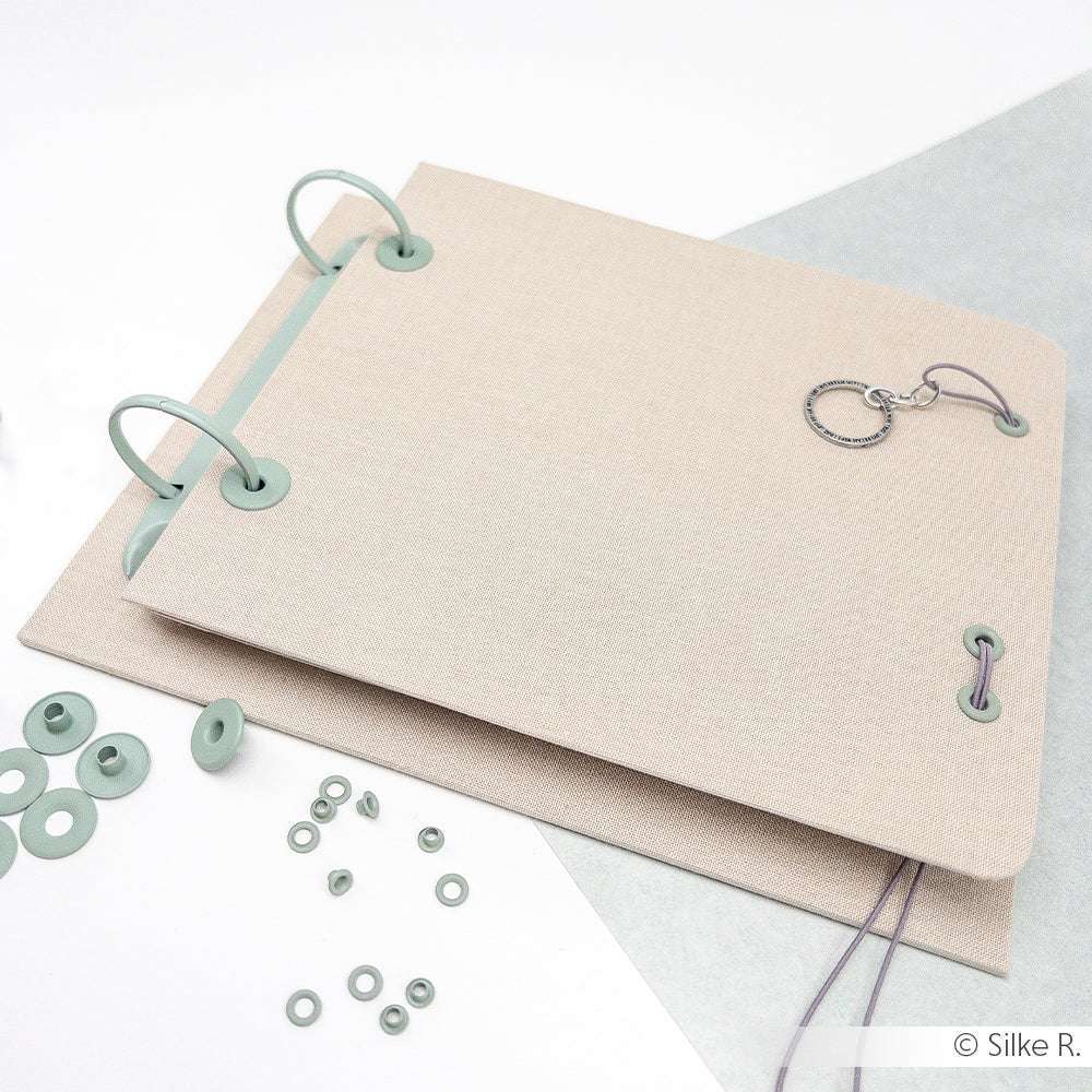 Zwei beige Ringbücher von Alexandra Renke mit Jaspisgrün-Ringen und eingestreuten Ösen mit Unterlegscheibe auf weißer Oberfläche - ideal für alle Ihre Buchbinden-Projekte.