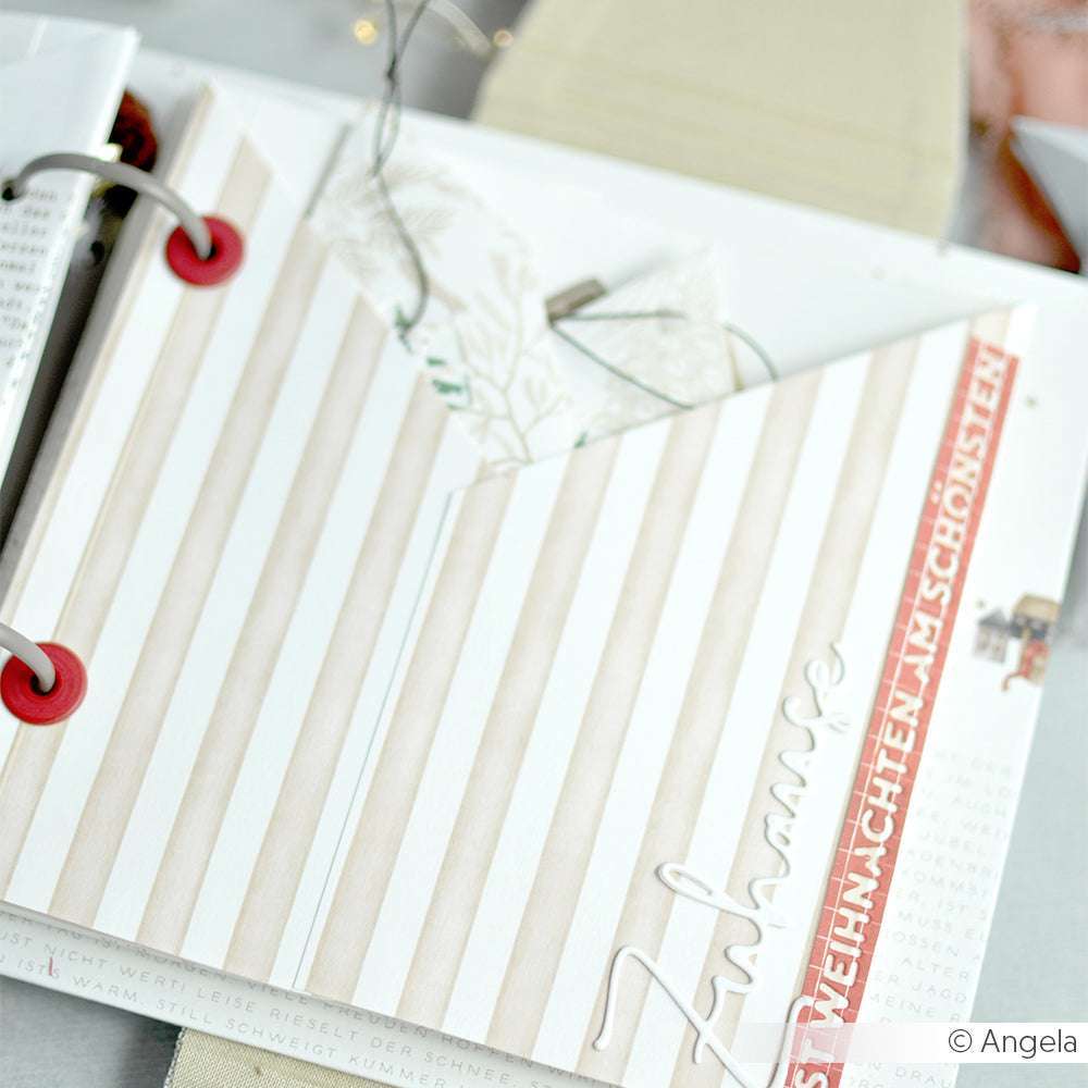 Das offene Scrapbook von Alexandra Renke hat gestreifte Seiten, Premiumrot-Akzente, "Zuhause" in Schreibschrift und ist mit Ösen mit Unterlegscheibe versehen.