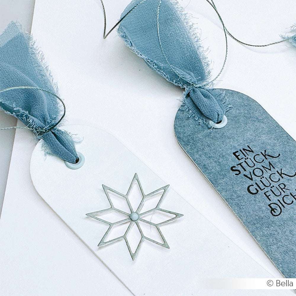 Zwei Lesezeichen von Alexandra Renke mit blauen Feenblau-Stoffbändern: eines mit silbernem Stern und Öse, das andere mit deutschem Text und minimalistischem Design - ideal für Buchbinden-Liebhaber.