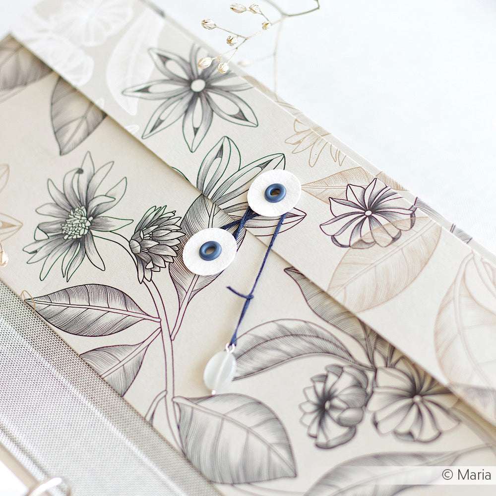 Alexandra Renke floraler Briefumschlag in Kosmosblau mit Kordelverschluss und Ösen, mit eleganten Blumen und Blättern in Line Art, auf einer hellen Oberfläche.