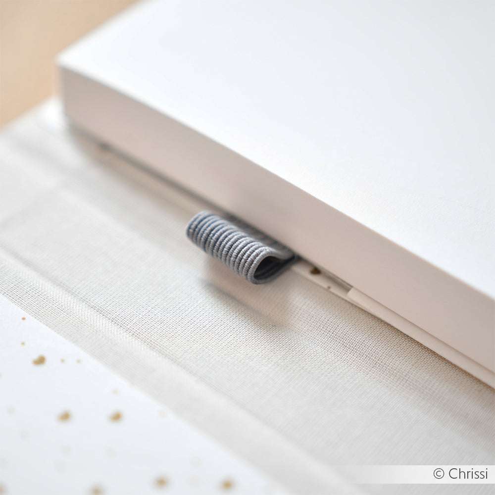 Ein grauer Stoffstifthalter mit Gummizugschlaufe aus ☆ ist an einem weißen Notizbuch befestigt, das auf einer hellen Fläche liegt.