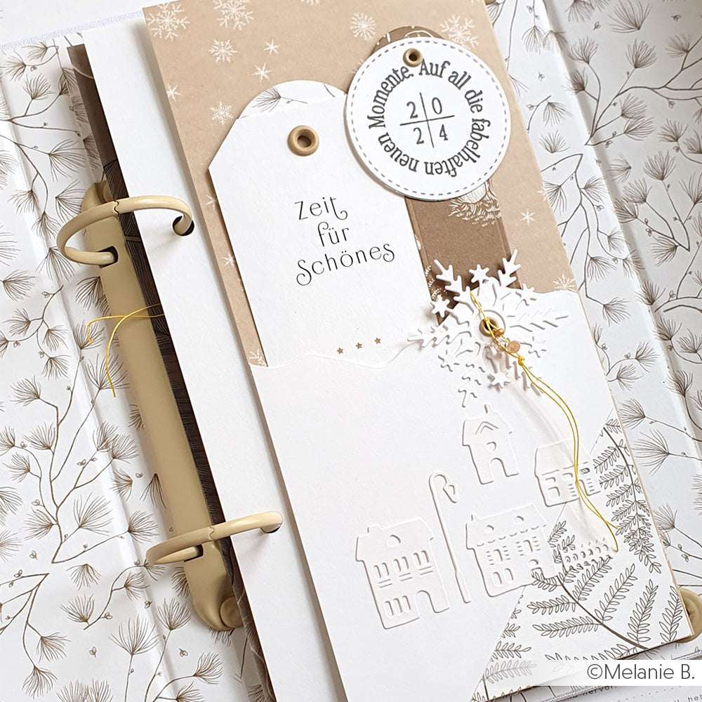 Elegante Winterkarte von Alexandra Renke mit geprägten Häusern, Schneeflocken und deutschem Text auf einem dekorativen Einband mit Ringbuchmechanik - ideal für Mini-Alben oder einzigartige Buchbindeprojekte.