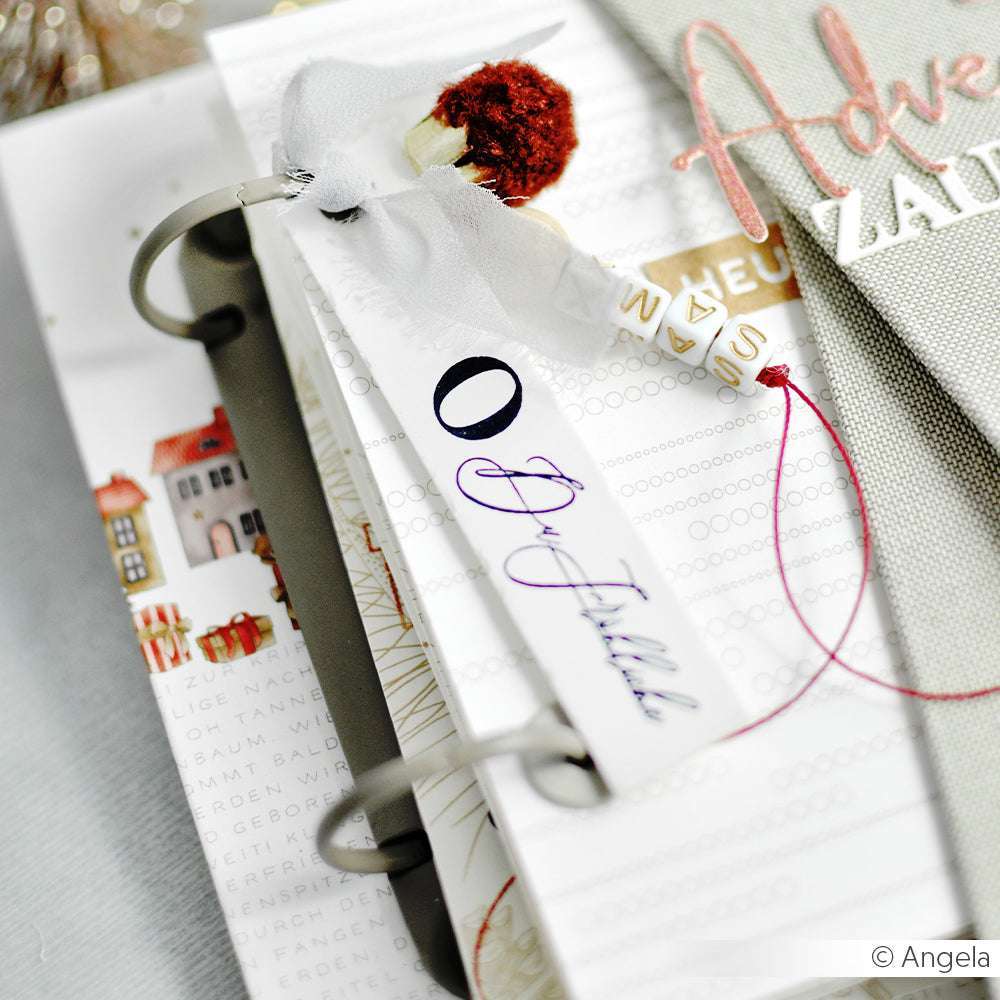 Eine Nahaufnahme eines dekorativen Anhängers mit Band und einer Blume, der an einem Alexandra Renke Ringbuchmechanik-Scrapbook befestigt ist, perfekt als Inspiration für Ihre Mini-Alben oder Buchbindungsprojekte.