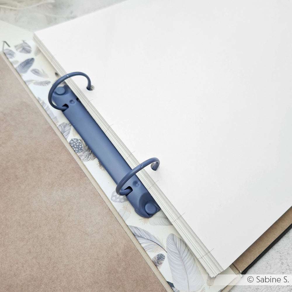 Offener Ordner von Alexandra Renke mit blauen Ringen, weißen Blankoseiten und einer federgemusterten Trennwand - ideal für Buchbindeprojekte oder zum Organisieren von Mini-Alben mit seiner stabilen Ringbuchmechanik.