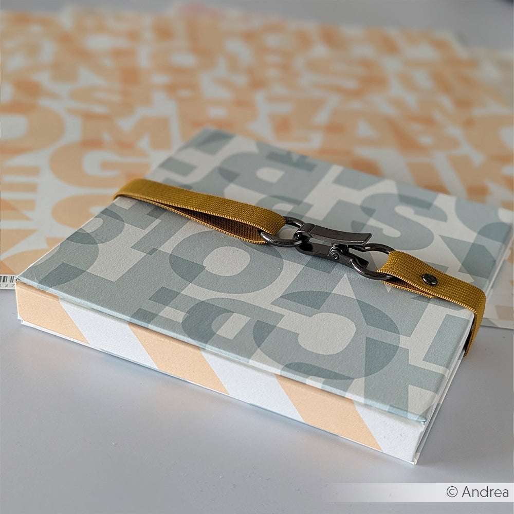 Alexandra Renke Box mit großen Buchstaben und einem gelben Blockstreifen Gelb, auf einem passenden Hintergrund aus Bucheinbandpapier.