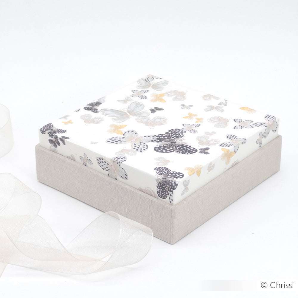 Quadratische Geschenkschachtel von Alexandra Renke mit einem Deckel aus Designpapier mit Schmetterlingsmuster und einem beigen Boden, der neben einer durchsichtigen Schleife auf weißem Hintergrund steht.
