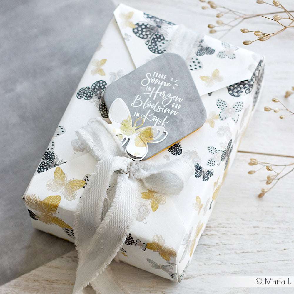 Als Geschenk verpackt in Alexandra Renke Schmetterling Bucheinbandpapier mit Stoffschleife und grauem Anhänger mit deutschem Text und Schmetterlingsmotiv - ideal für kreative Buchbinden oder besondere Designpapierprojekte.