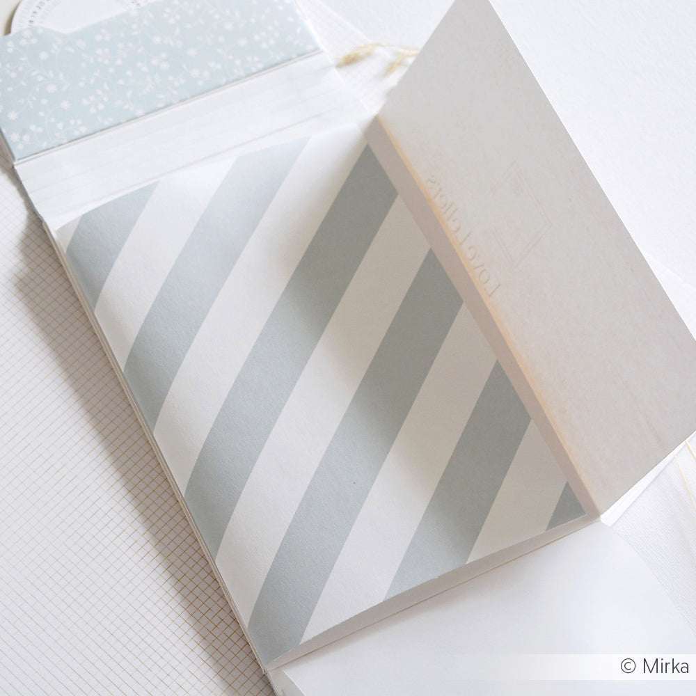 Ein offener Notizblock von Alexandra Renke mit diagonal hellblau-weiß gestreiften Seiten, ideal zum Buchbinden oder zum Aufwerten von Projekten mit einem Hauch von elegantem Designpapier.