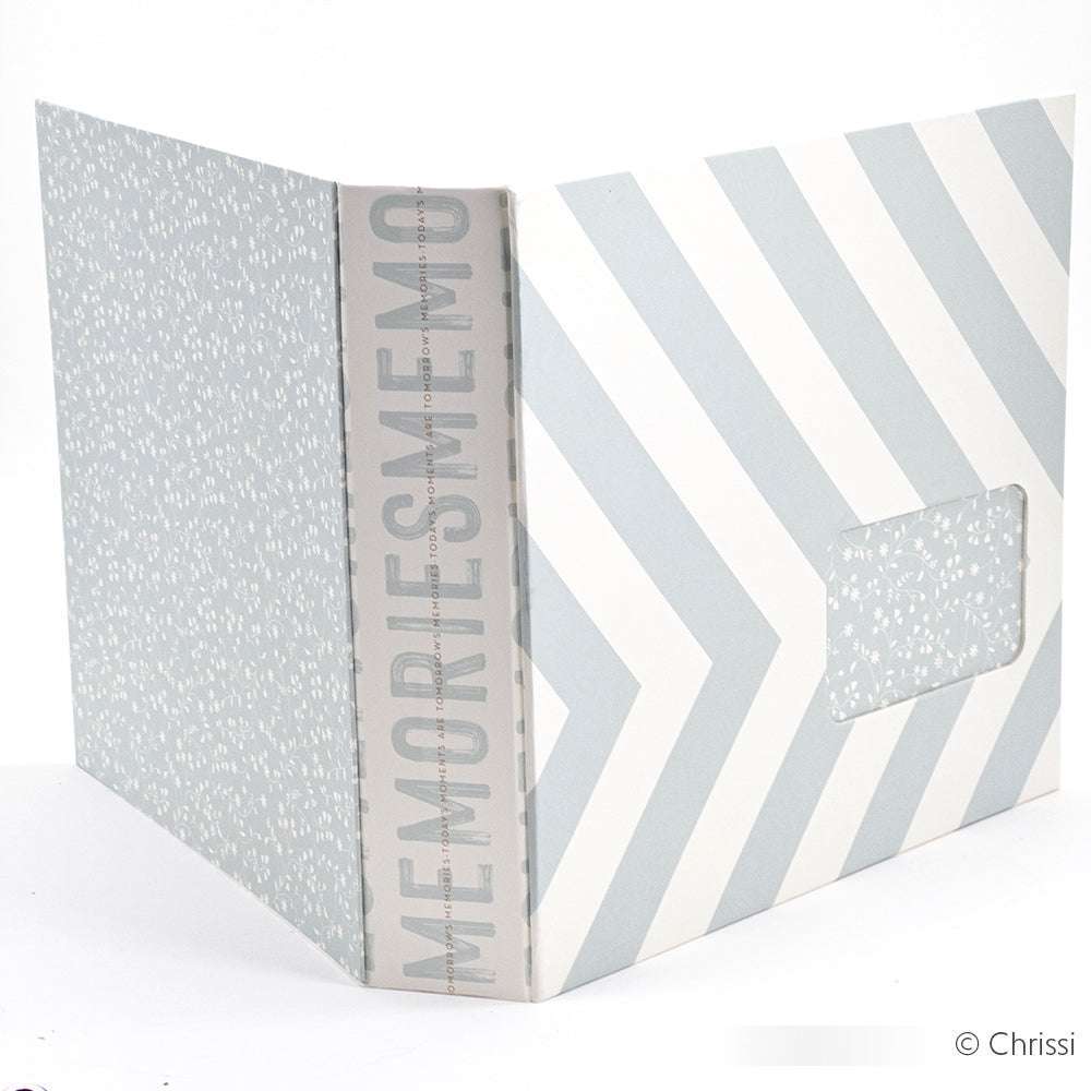 Ein hellblau-weißes, chevrongemustertes Fotoalbum von Alexandra Renke mit MEMORIES auf dem Rücken, einem kleinen Einbandfenster und aus hochwertigem Bucheinbandpapier.
