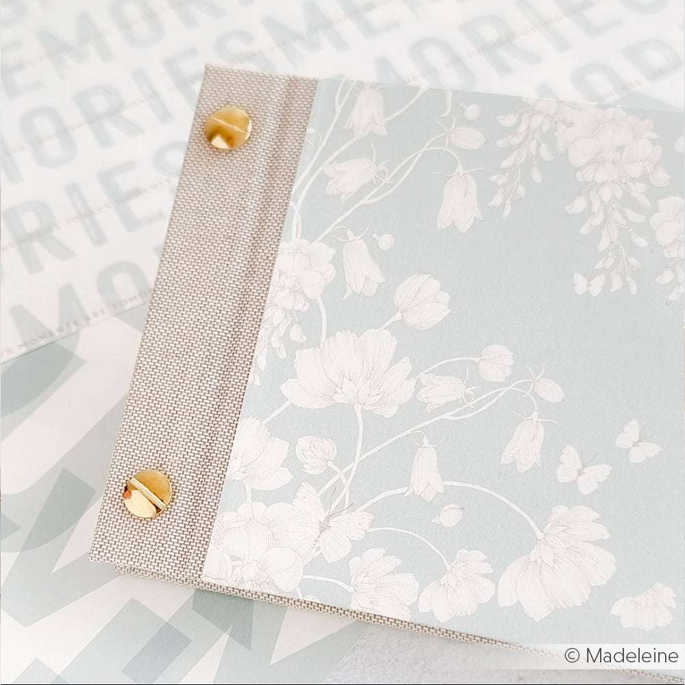 Nahaufnahme eines floral gemusterten Binders von Alexandra Renke mit goldenen Verschlüssen auf einer MEMORIES-Oberfläche - ideal für kreatives Buchbinden und die Darstellung von Blumenharmonie auf Blau.