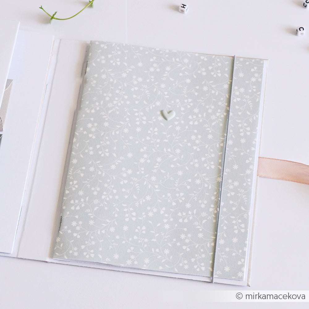 Ein blassblaues, geblümtes Notizbuch von Alexandra Renke mit einem kleinen Herz-Detail, gefertigt aus elegantem Bucheinbandpapier, liegt aufgeschlagen auf einer weißen Fläche.