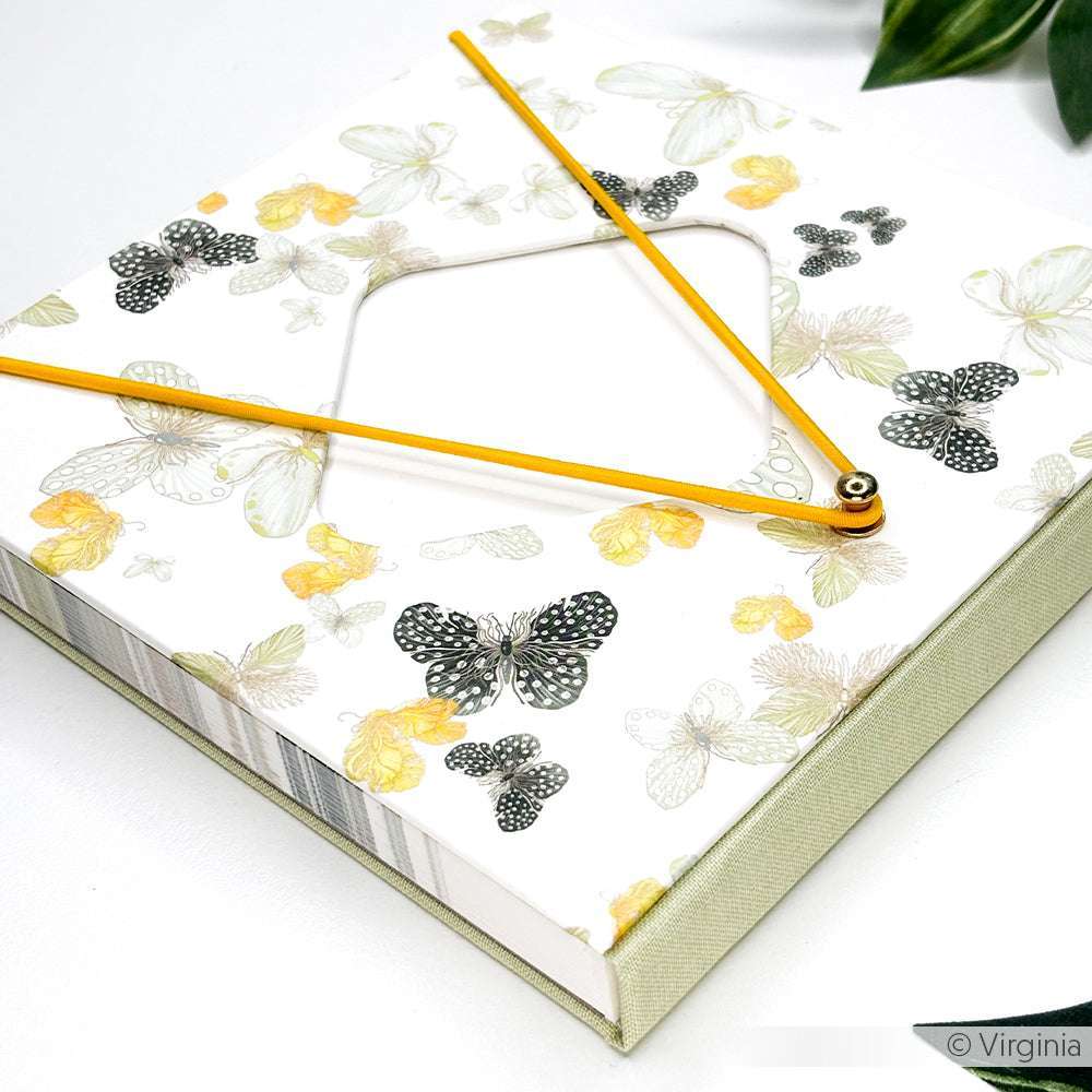 Das quadratische Skizzenbuch von Alexandra Renke hat einen Einband aus Bucheinbandpapier mit Schmetterling und einen gelben Zirkel auf der Oberseite, der auf einer weißen Fläche mit grünen Blättern liegt - ideal für kreatives Buchbinden oder das Gestalten mit einzigartigem Designpapier.