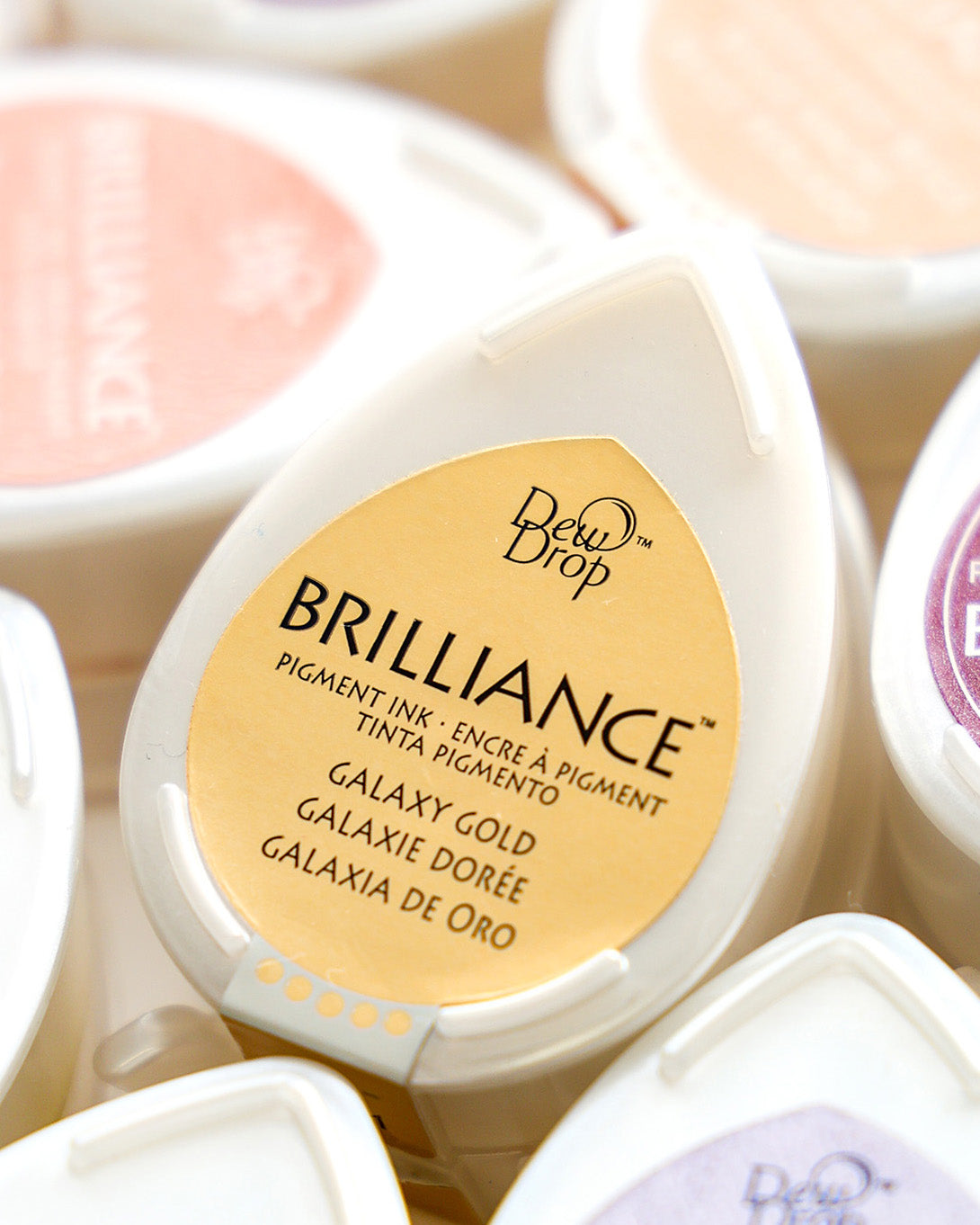 Nahaufnahme eines Brilliance Dew Drop Stempelkissens mit der Aufschrift Galaxy Gold zwischen anderen bunten Stempelkissen.