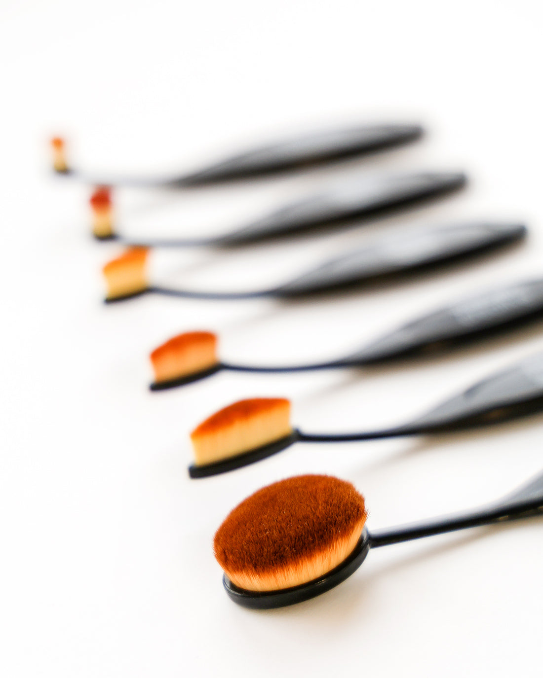 Ein Satz ovaler Make-up-Pinsel, die in einer Reihe auf einem weißen Hintergrund angeordnet sind, dargestellt mit Weichzeichner.