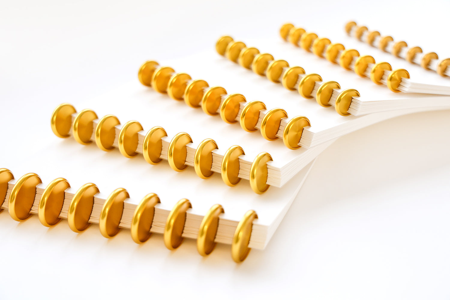 Fünf Notizbücher mit goldenen Scheibeneinbänden sind in einem diagonalen Muster auf einer weißen Fläche angeordnet.