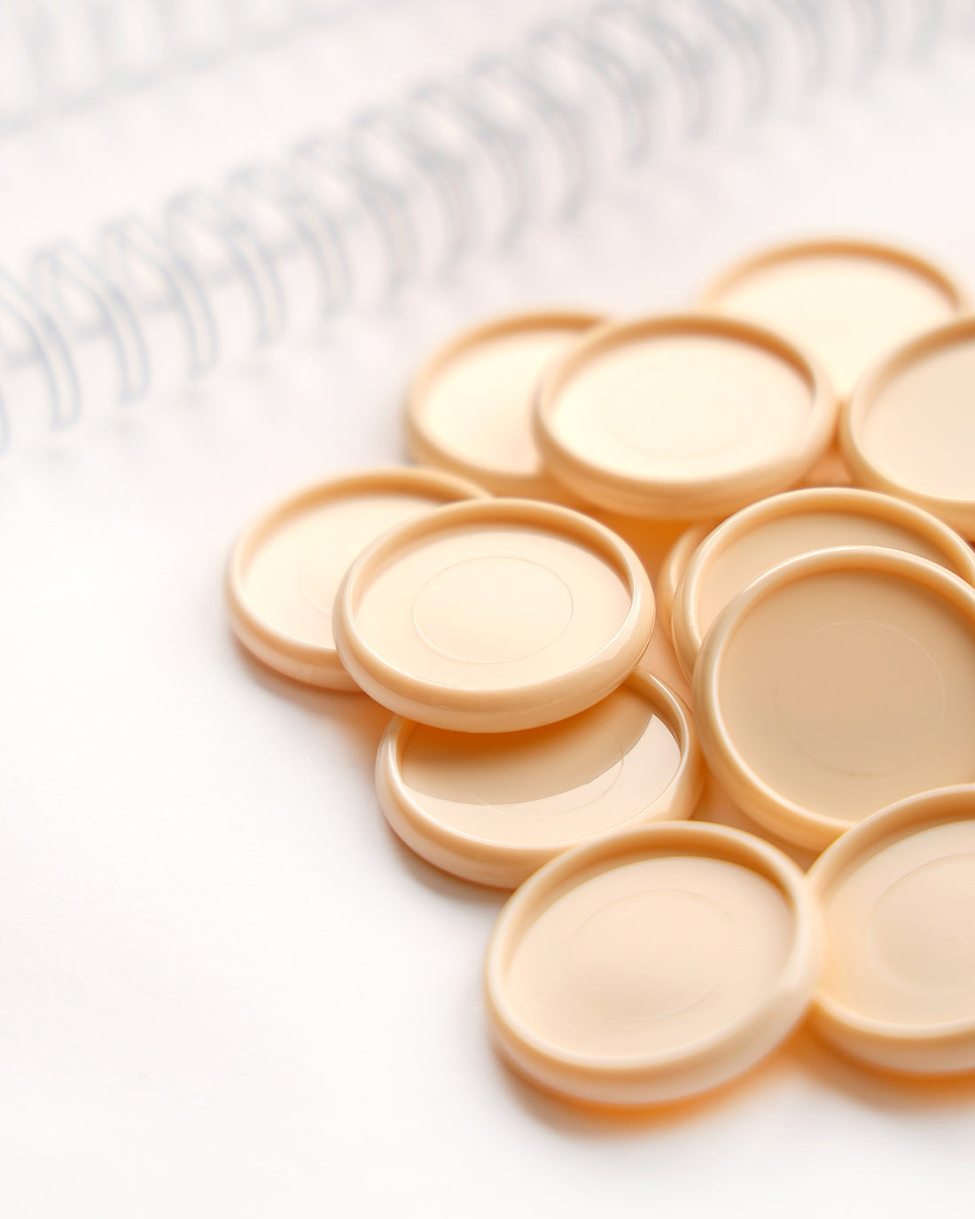 Ein Stapel beigefarbener runder Plastikdeckel auf einer weißen Fläche, mit einem Spiralheft im Hintergrund.