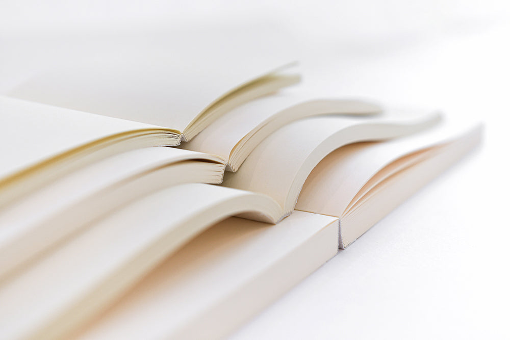 Vier aufgeschlagene leere Bücher sind dicht nebeneinander gestapelt und zeigen gebogene Seiten und weiße Hintergründe.