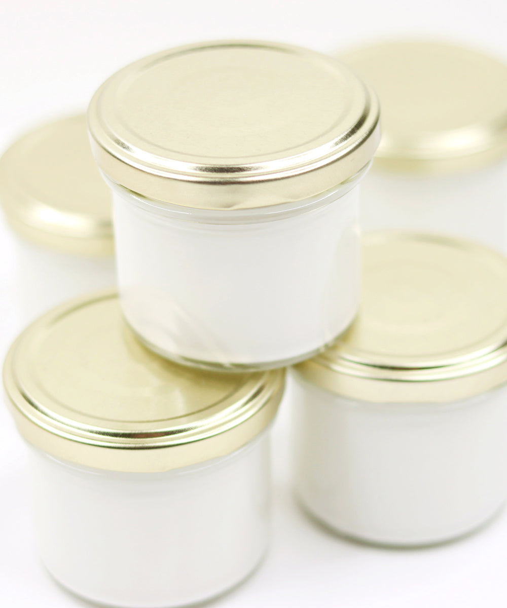 Vier kleine Gläser mit goldenen Deckeln, gefüllt mit einer weißen, cremigen Substanz, dicht nebeneinander angeordnet.