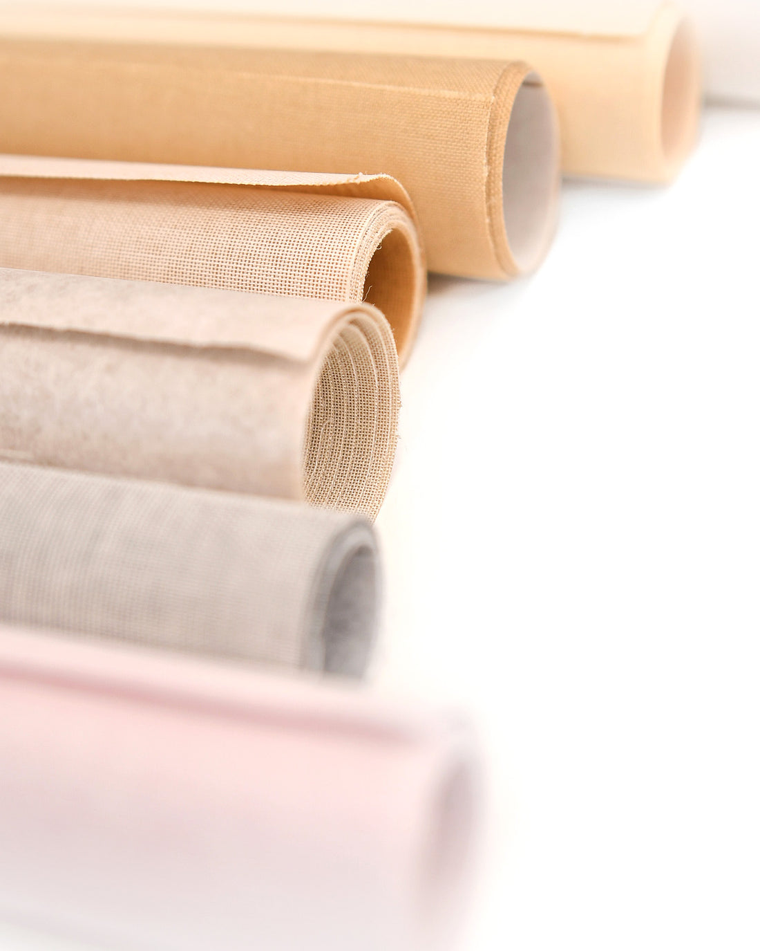 Aufgerollte Stoffe in neutralen Beige-, Creme- und sanften Pastelltönen auf weißem Hintergrund.
