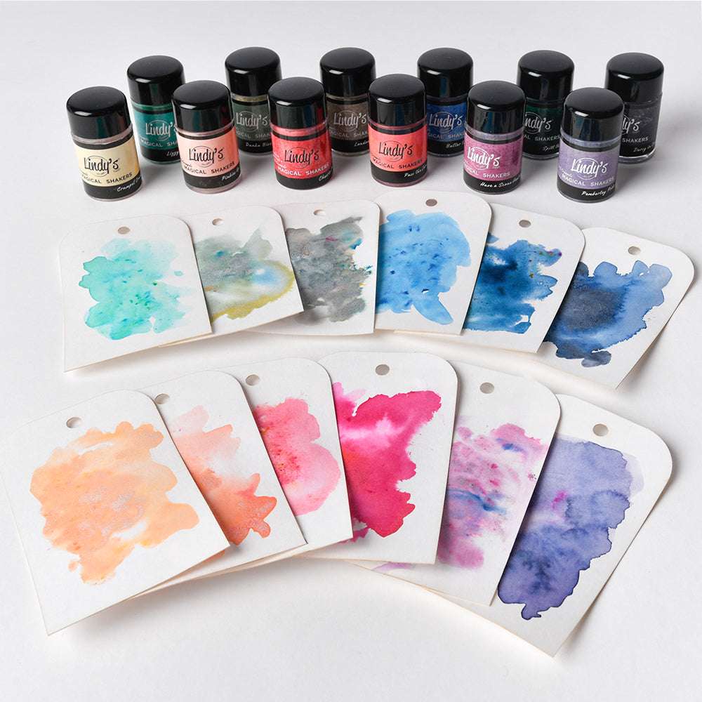 Lindy's Stamp Gang Magical Powder-Gläser mit bunten Aquarellmustern sind vorne ausgestellt und heben wunderschöne Farbmischungen und brillante Effekte hervor.