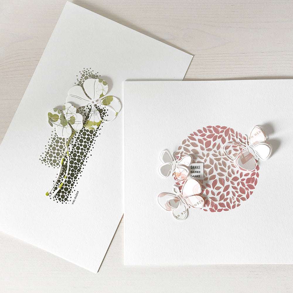 Zwei The Crafters Workshop-Grußkarten mit 3D-Schmetterlingsmotiven und Blumenausschnitten auf einer hellen Holzoberfläche - ideal für Mixed-Media-Projekte.