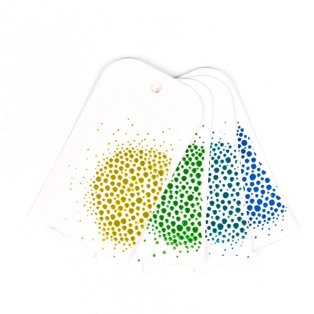 Vier weiße Anhänger von The Crafters Workshop mit gepunkteten Mustern in Gelb, Grün, Petrol und Blau sind auf einer weißen Fläche aufgefächert - ideal zum Hinzufügen von Stencil Butters oder Modellierpaste, um Ihr nächstes Mixed-Media-Projekt zu inspirieren.