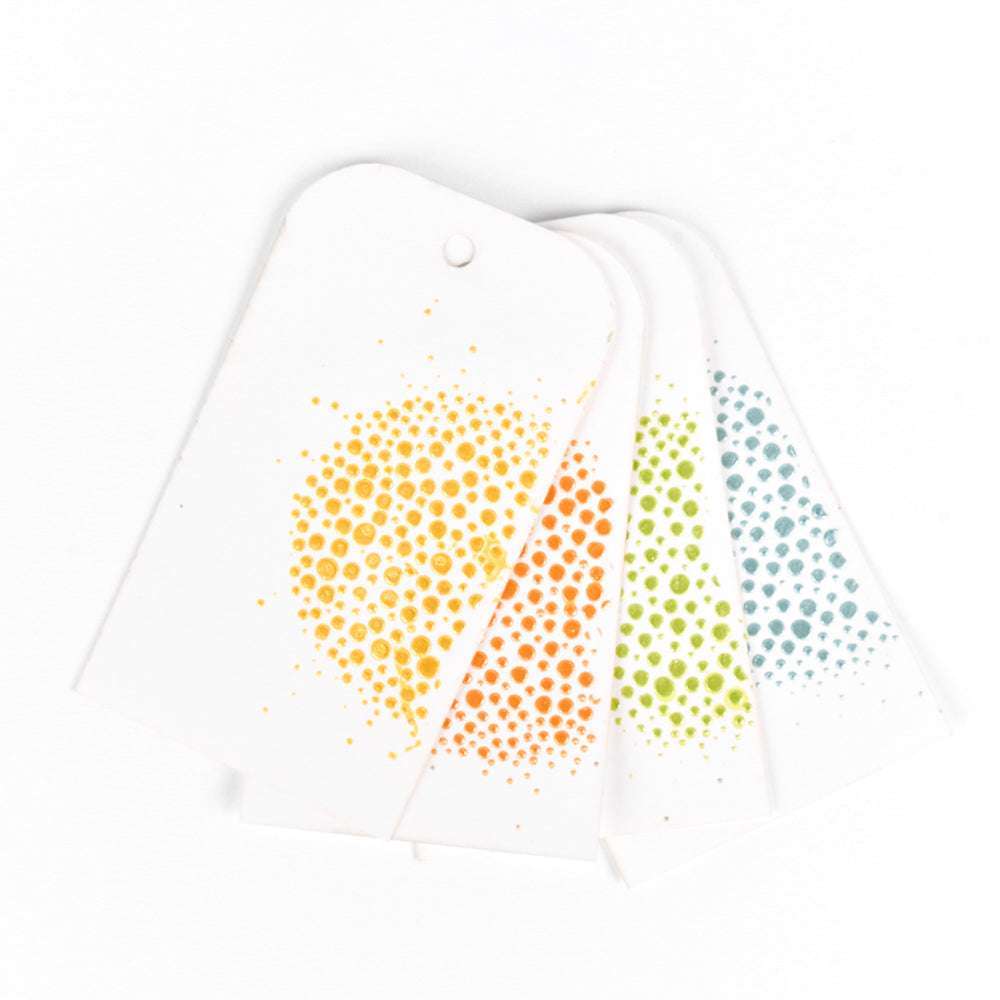 Vier weiße Geschenkanhänger von The Crafters Workshop mit bunten gepunkteten Kreisen in Gelb, Orange, Grün und Blau sind auf einer weißen Fläche aufgefächert - perfekt für Ihr nächstes Mixed-Media-Projekt.