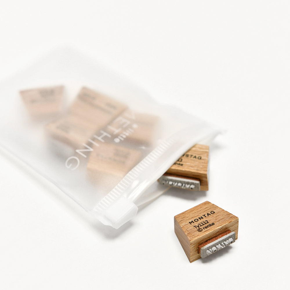 Kleine Holzstempel aus dem Alexandra Renke Mini Typo Holzstempel Set, mit Metalletiketten, sind teilweise sichtbar in einem gefrosteten Plastikbeutel mit Reißverschluss auf einer weißen Oberfläche.