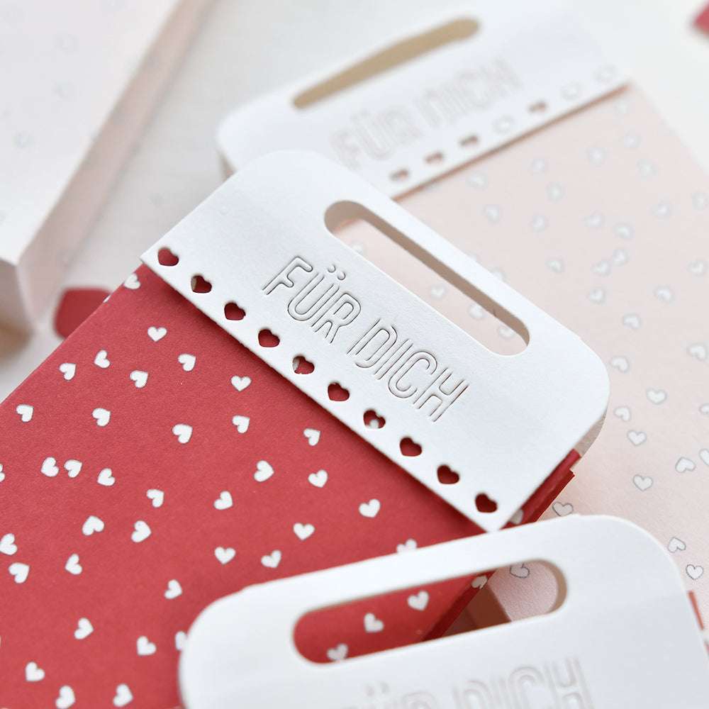 Rote und rosafarbene Alexandra Renke Geschenktüten mit weißen Herzen und dem Schriftzug "FÜR DICH" an den Henkeln - ideal zum Verpacken von Inspirationsgeschenken oder zum Herstellen eines eigenen Geschenkpakets.