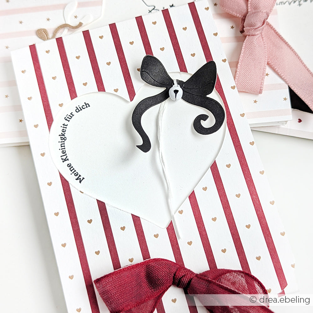 Grußkarte von Alexandra Renke mit einem gestreiften Herz mit deutschem Text, goldgepunktetem Hintergrund, schwarzer Schleife und weinrotem Band - einzigartig und kreativ elegant.