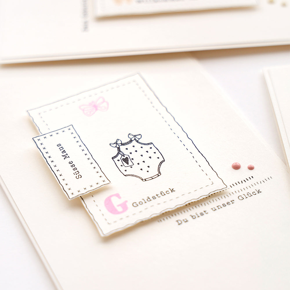 Eine handgemachte Karte von Alexandra Renke mit einem Baby-Strampler, rosa Punkten und "G Goldstück" & "Süßes Baby" - ideal für kreative Sammlungen oder als Teil eines liebevollen Pakets.
