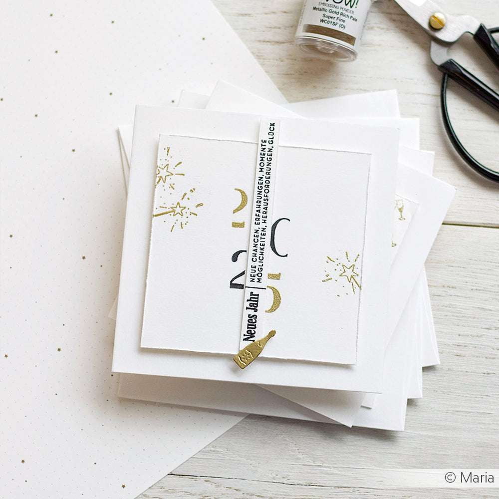 Ein Stapel creme-weißer Ton Umschläge und Karten mit goldenen und schwarzen Akzenten, Scheren und gepunktetem Papier aus der Alexandra Renke Hauskollektion auf einer weißen Fläche.