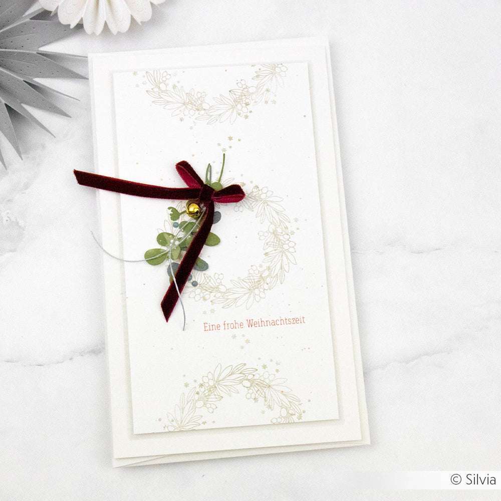 Elegante Weihnachtskarte von Alexandra Renke mit Umschlag, verziert mit rotem Band, goldener Glocke und Grün auf cremeweißem Karton. Enthält deutschen Text.