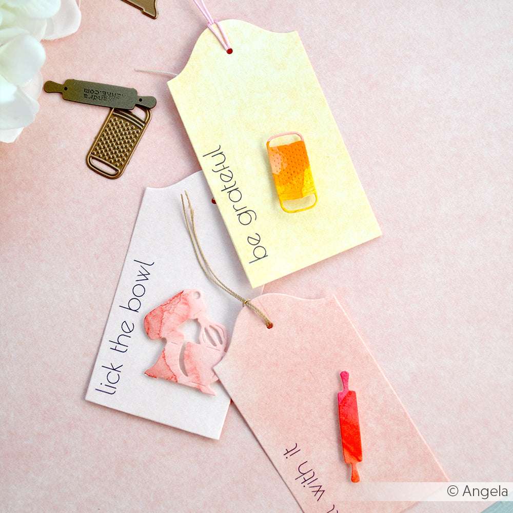 Drei pastellfarbene Geschenkanhänger mit Dekorationen und Botschaften zum Thema Backen auf einer rosafarbenen Oberfläche - perfekt für ein charmantes Bündel, das die Kreativität anregt, von Alexandra Renke.