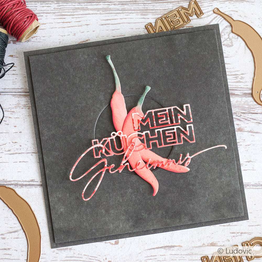 Quadratische Karte aus Alexandra Renke-Papier mit roten Chilischoten und dem Text "MEIN KÜCHEN Geheimnis" auf dunklem Hintergrund.