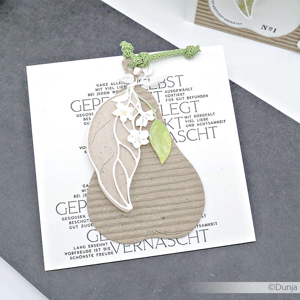 Eine handgefertigte birnenförmige Karte mit floralen Details ruht auf einer weißen Karte von Alexandra Renke, die mit ihrem Clear Stamp Set "Aus meinem Garten" gestempelt wurde, mit deutschem Text im Hintergrund.