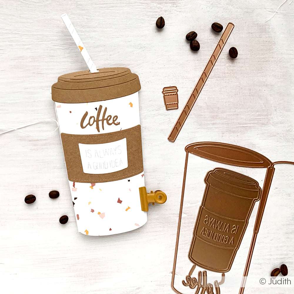 Eine Kaffeebecher-Bastelei aus Papier mit Kaffeebohnen, einem Rührstab, Designpapieren, Motivstanze und Metallstanzformen von Alexandra Renke wird auf einem weißen Hintergrund gezeigt.